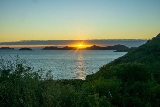 Breathtaking view of a tropical island sunset over a calm ocean with lush greenery.