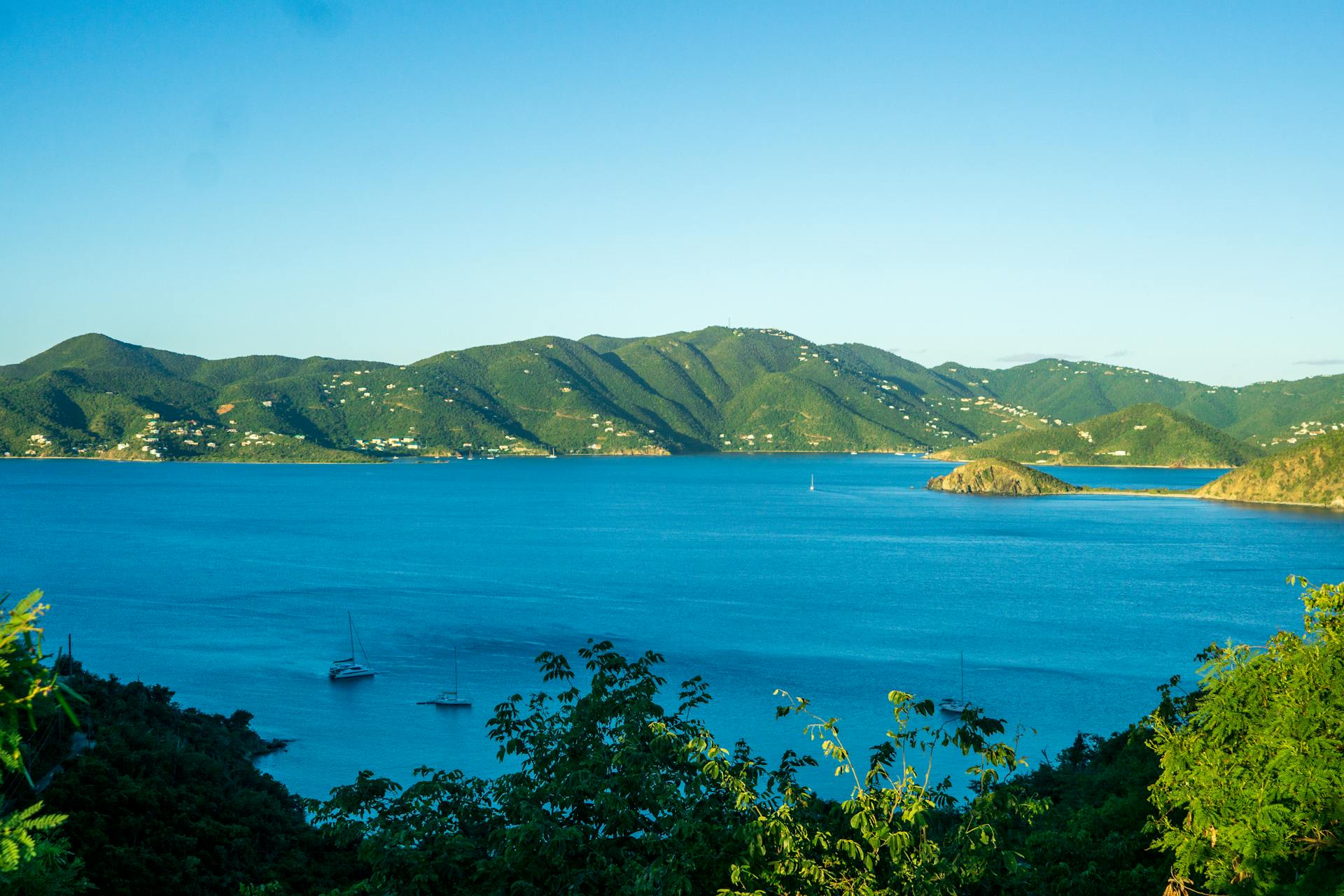 Scenic view of the Caribbean Sea with sailboats and lush mountains under clear blue skies.