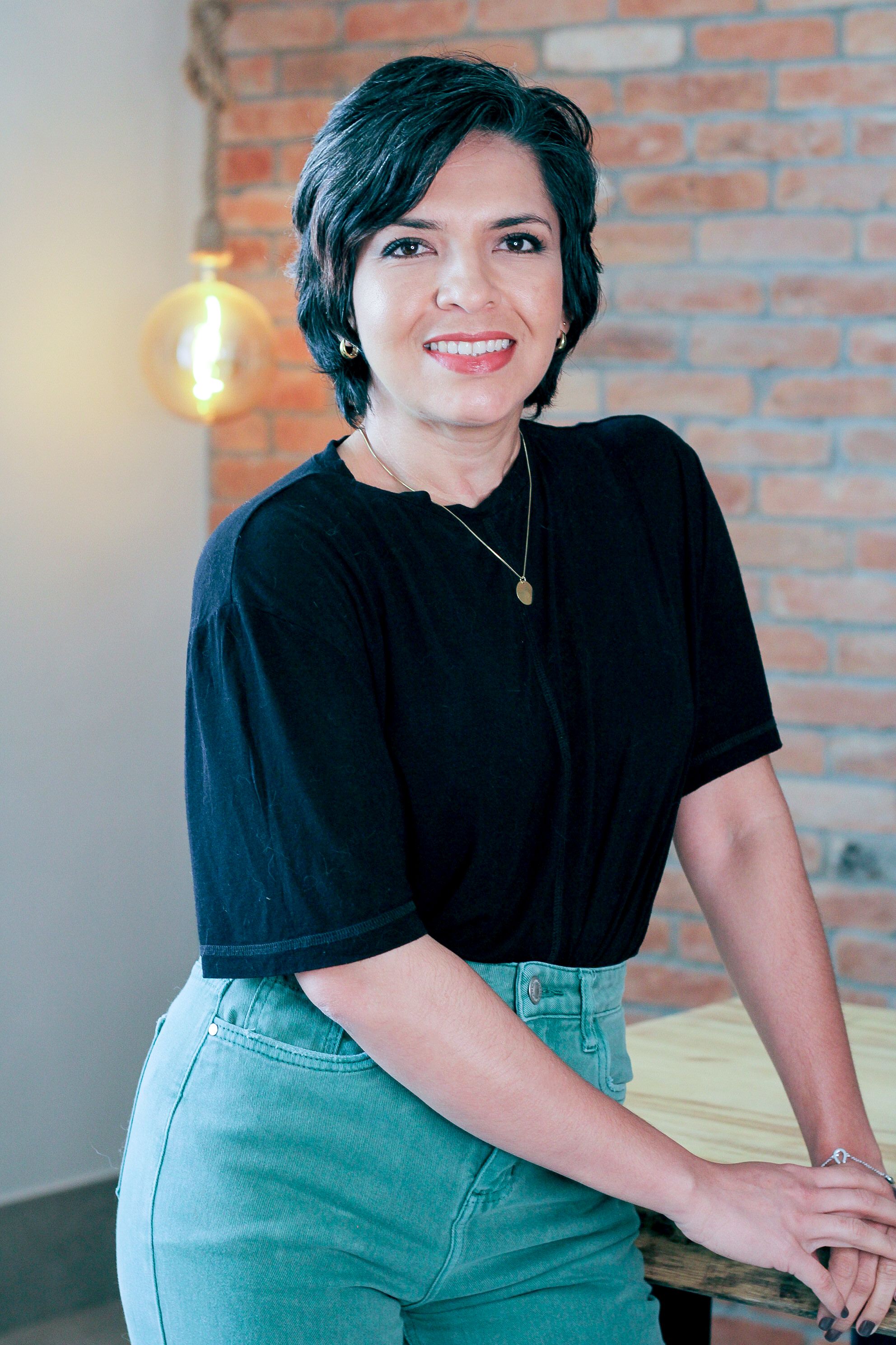 Casual portrait of a smiling woman with short hair against a brick wall.