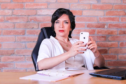 Woman Sitting at the Desk with an iPhone in her Hands 