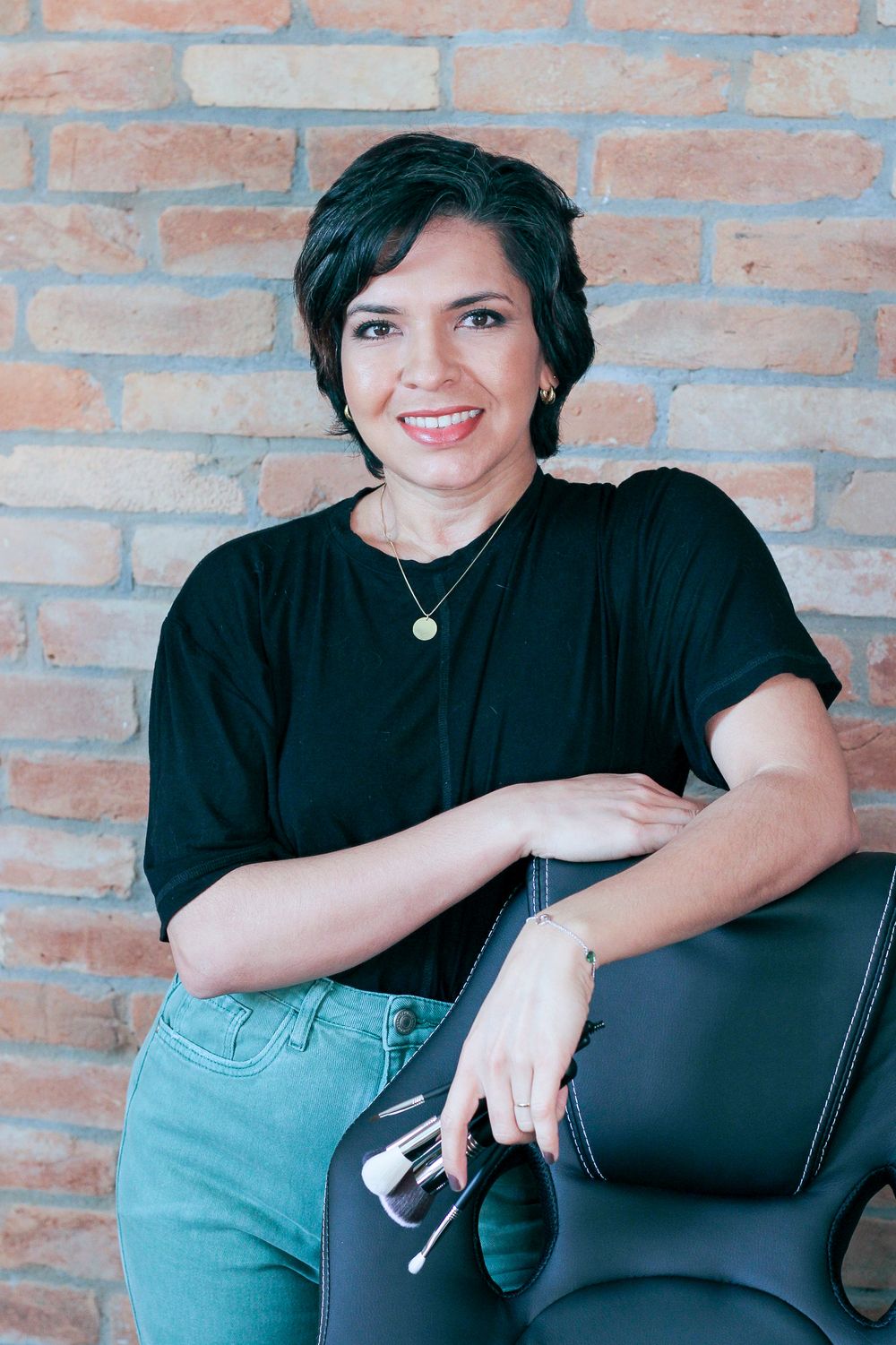 Founder in a black top with a makeup chair against a brick wall