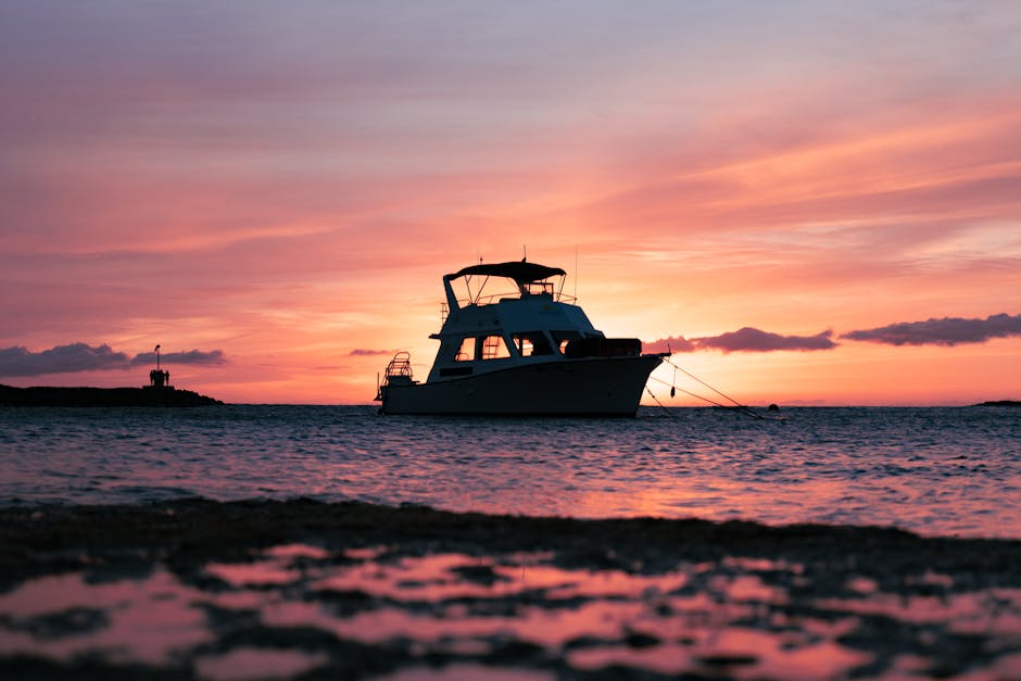 Photo by Colin Fearing A picturesque boat silhouette floats on the ocean at sunset with vibrant skies in Hanapepe, Hawaii.