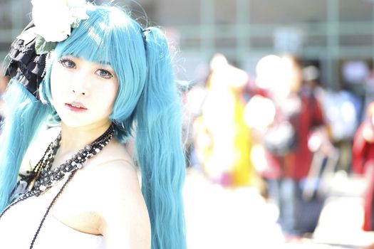 Vibrant cosplay portrait of a woman with blue hair and intricate costume in bright outdoor setting.