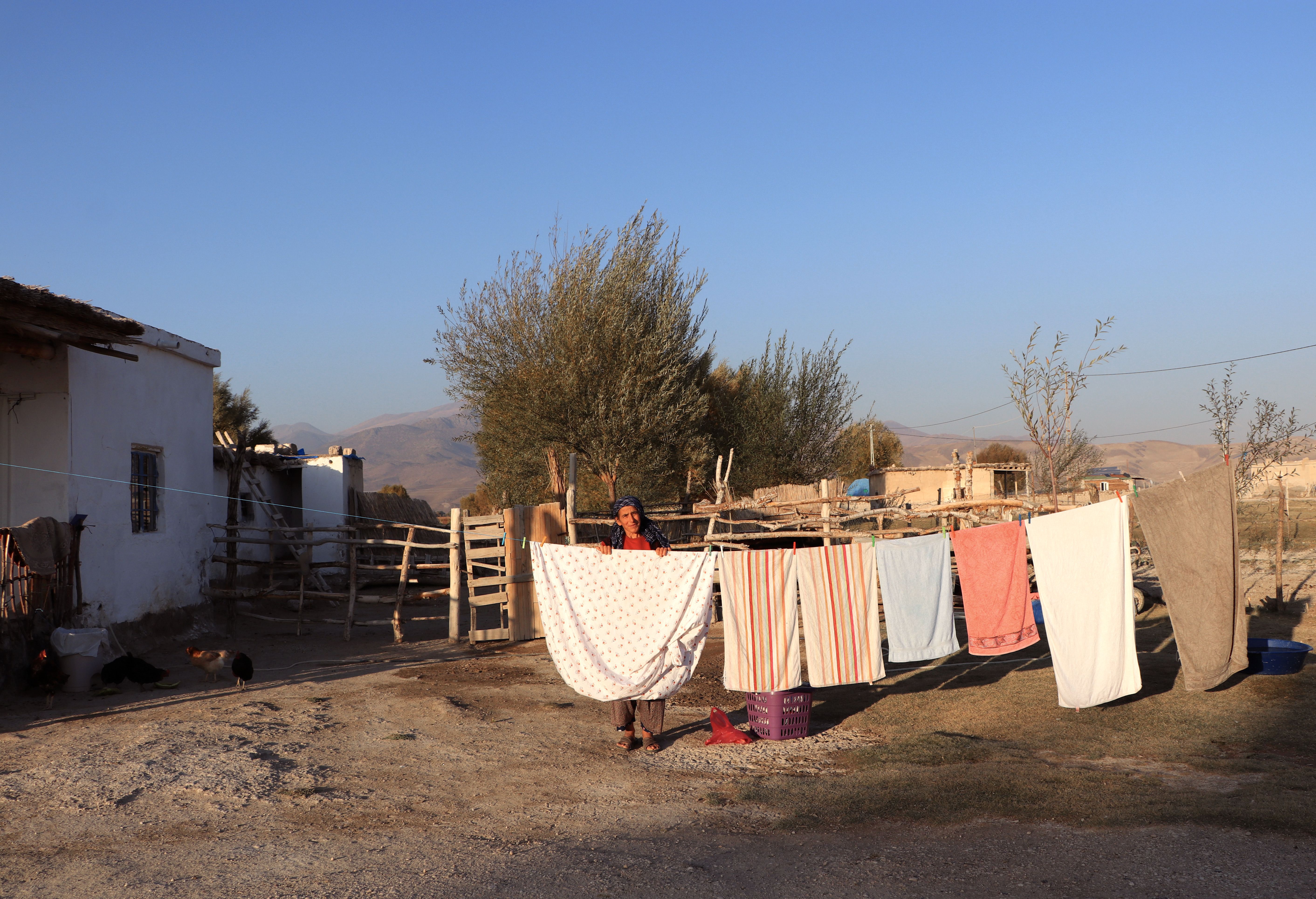 A woman hangs laundry on a clothesline in a rural setting under clear blue skies.