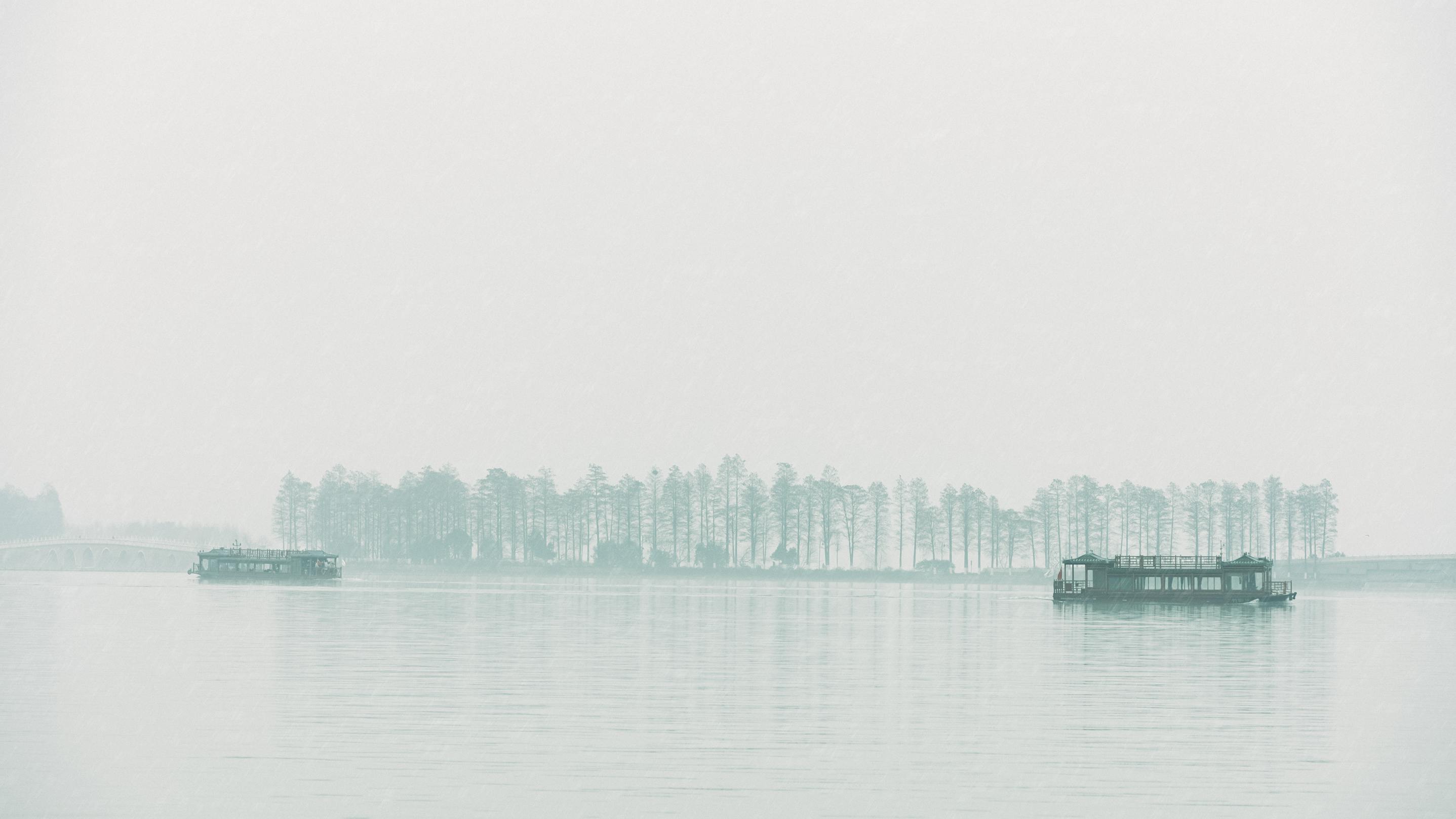 Tranquil scene of boats on a misty lake with hazy trees in the background.