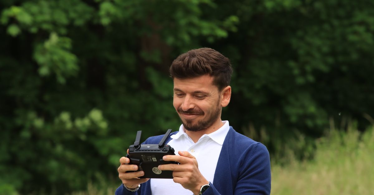Smiling man using drone controller outdoors in a lush green setting.