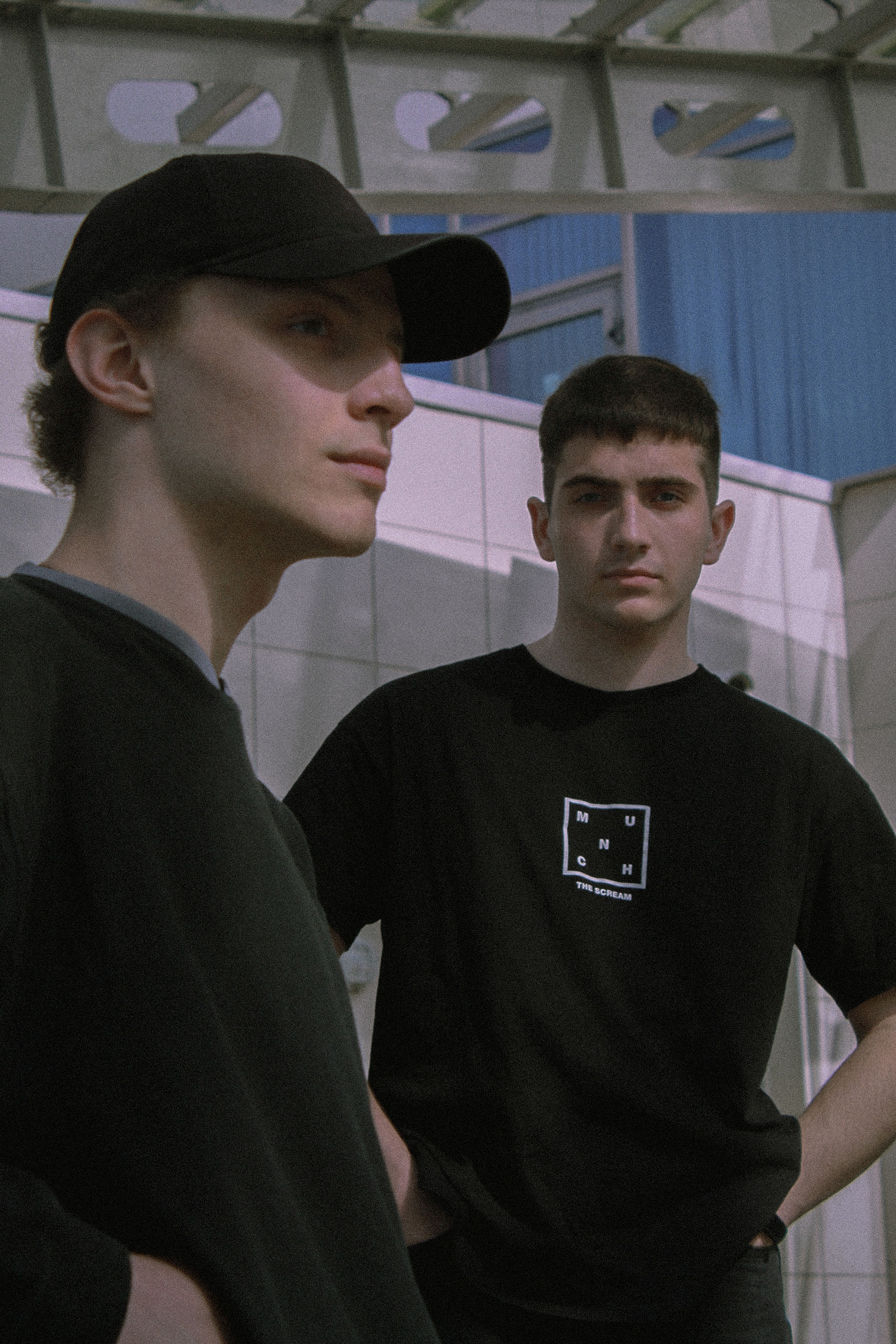 Two young men in black streetwear pose outdoors, embodying casual fashion.