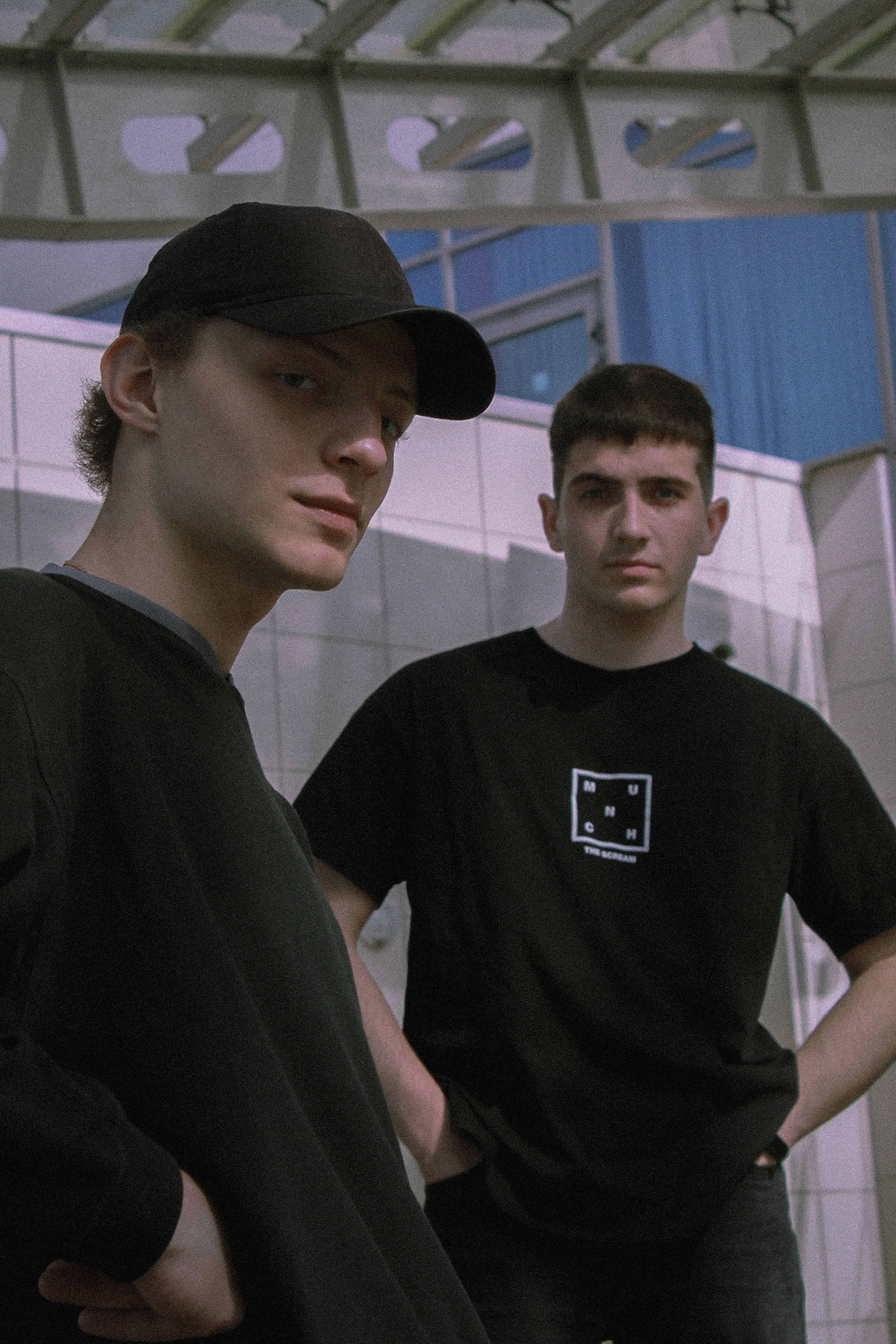 Stylish portrait of two young men in black attire standing outdoors with modern architecture.