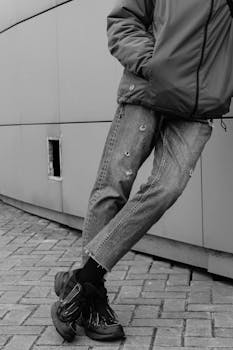 Stylish urban youth in jeans and sneakers on a city street wall.