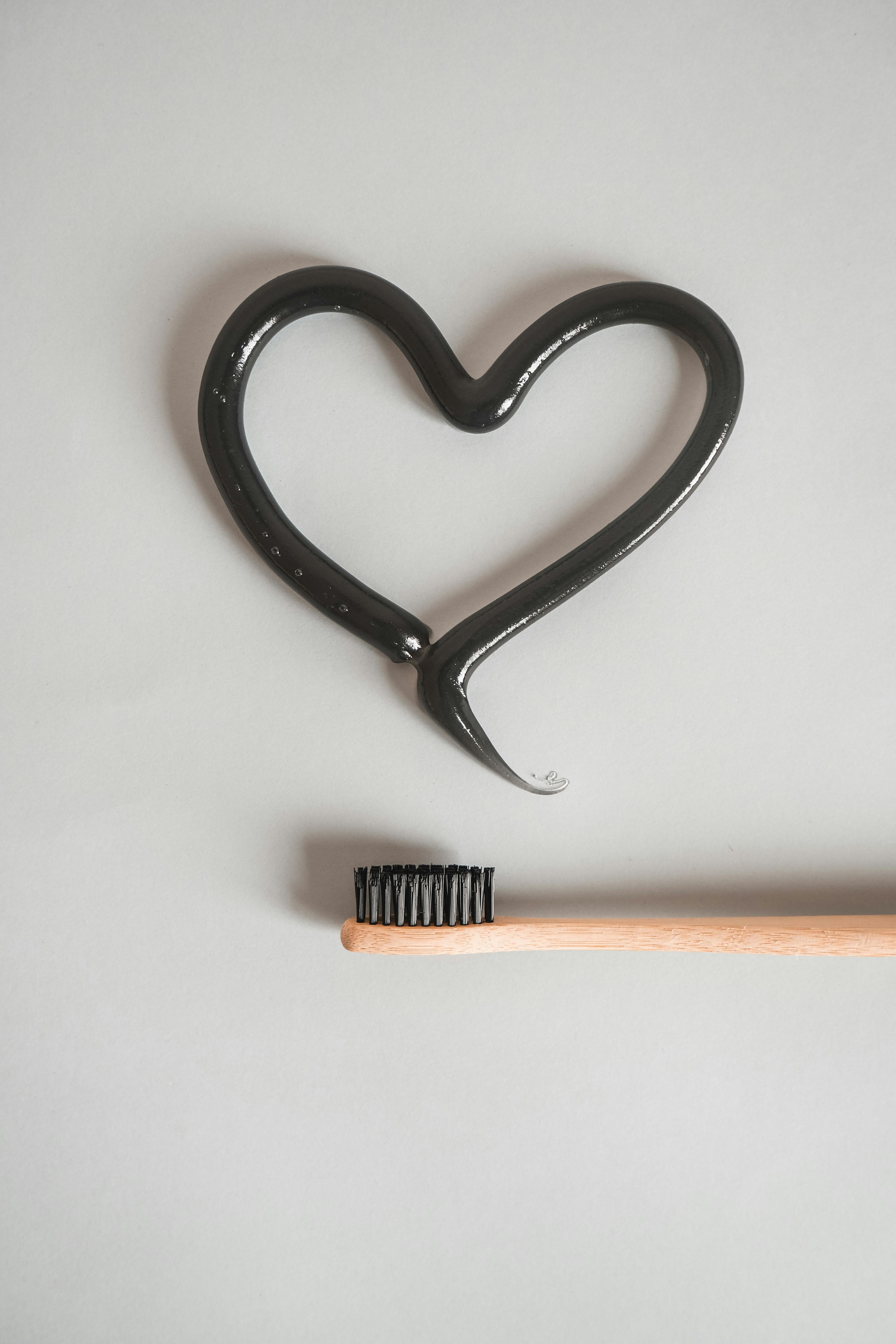 A wooden toothbrush with black bristles and heart-shaped charcoal toothpaste on a white background.