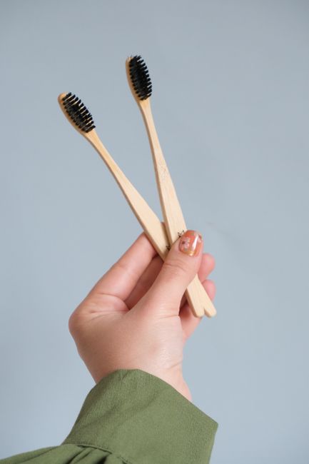 Close-up of hand holding two eco-friendly bamboo toothbrushes against blue background.