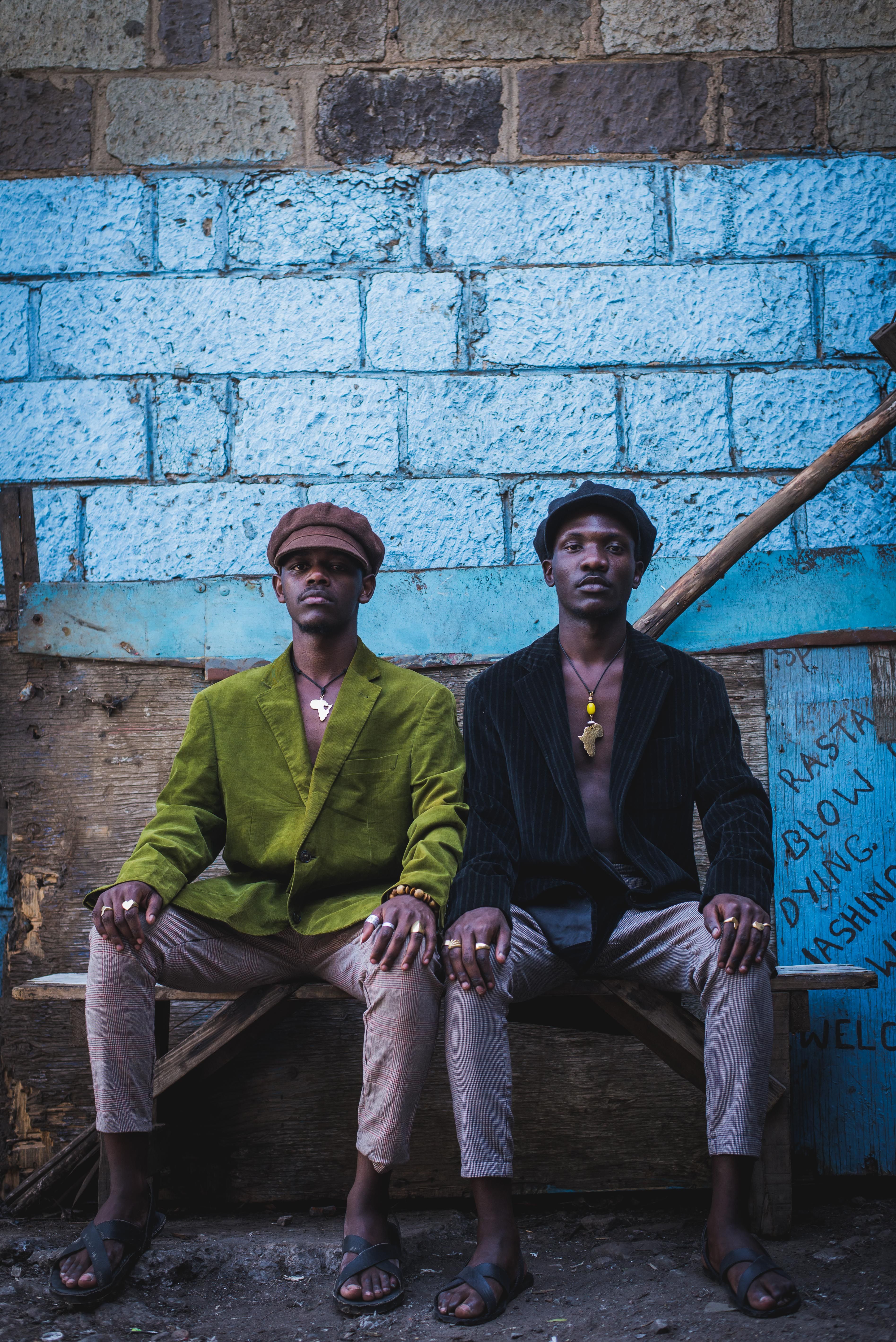 Two men sitting on a bench in front of a blue wall · Free Stock Photo