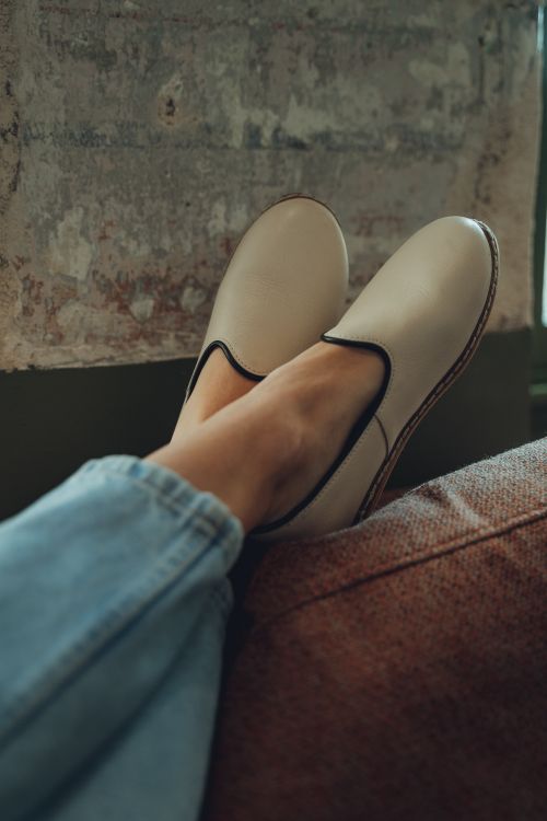 Free Person relaxing on a sofa wearing beige slip-on shoes and jeans, showcasing casual fashion. Stock Photo