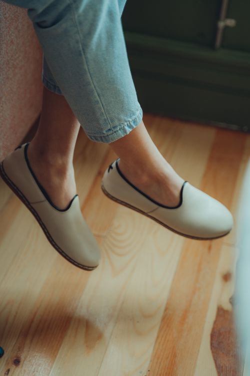 Free A close-up of a woman wearing casual shoes and jeans, dangling legs above a wooden floor. Stock Photo