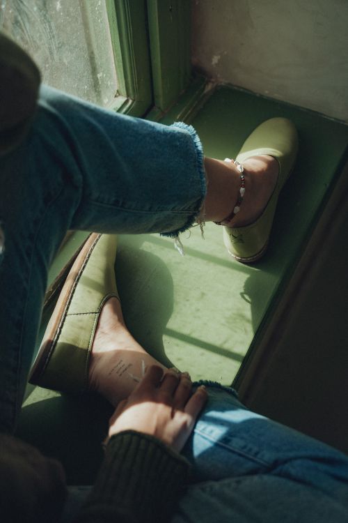 Free Woman sitting in sunlight, wearing jeans and green shoes, capturing a serene atmosphere. Stock Photo