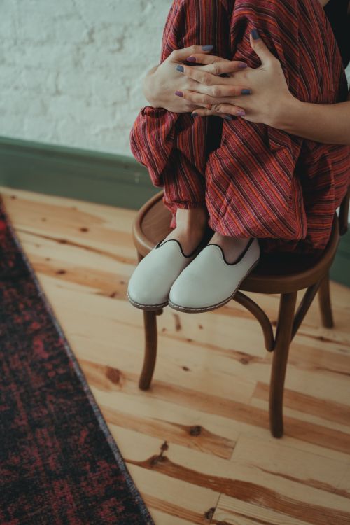 Free Woman in casual clothing sitting cross-legged on a chair indoors, displaying relaxed style. Stock Photo