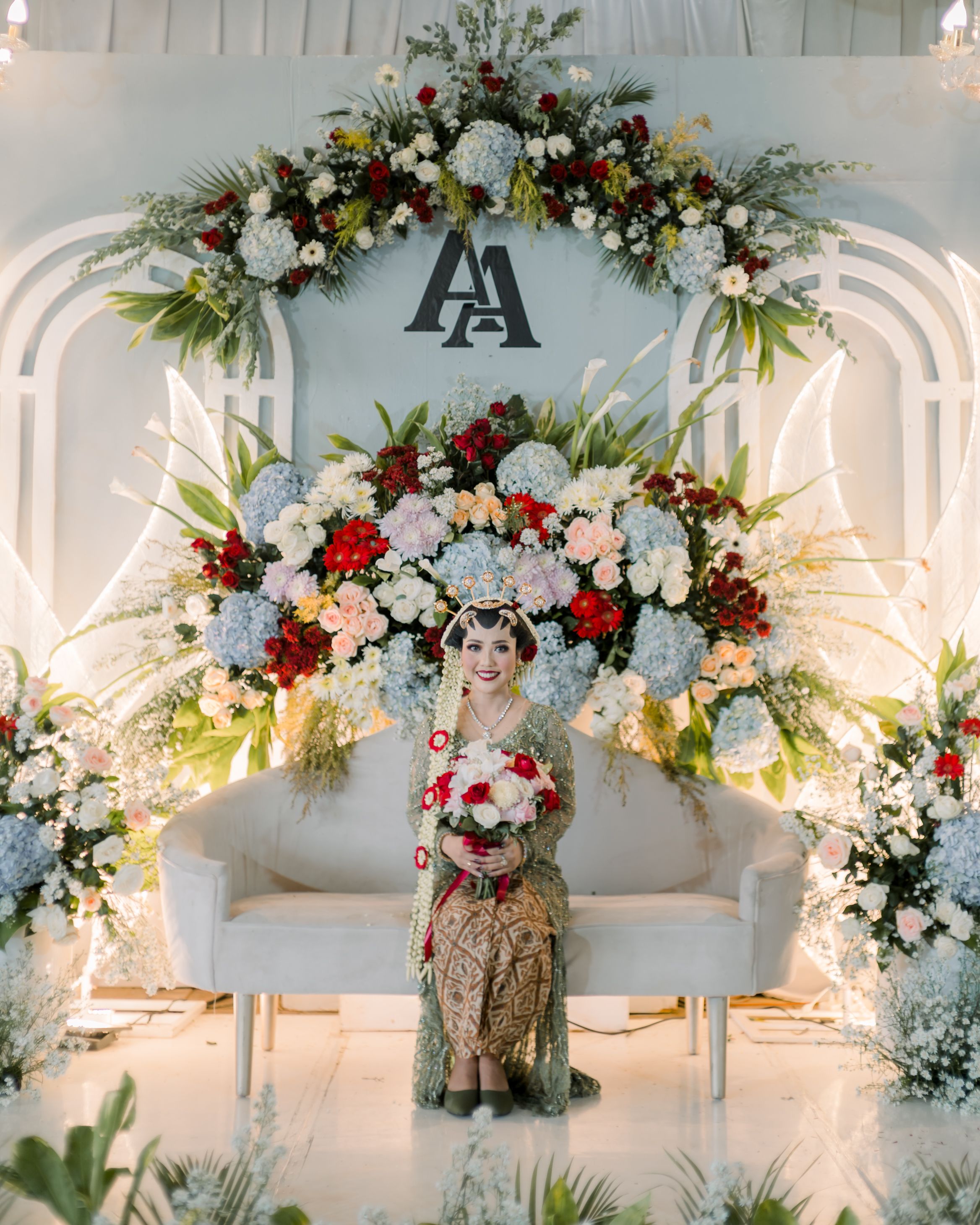 Beautiful Javanese bride in traditional attire with floral backdrop at wedding ceremony in Surakarta.