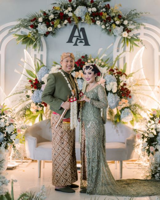 Couple in traditional attire posing in front of floral decorations at a wedding ceremony.