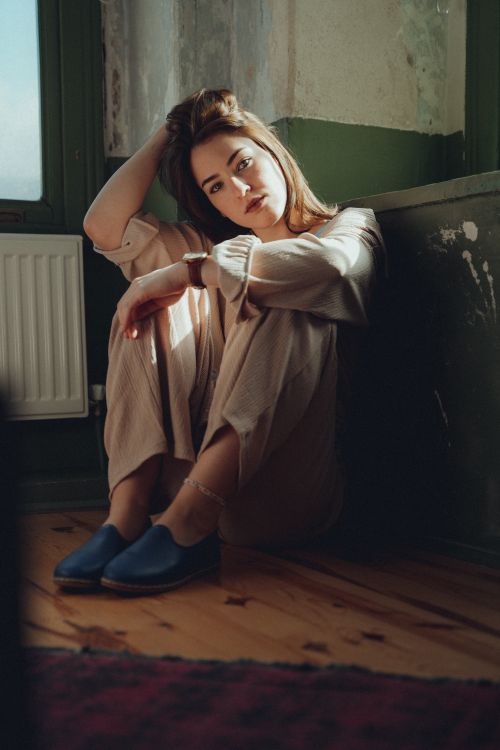 Free A young woman sitting thoughtfully on the floor in a sunlit indoor room, creating a serene and introspective mood. Stock Photo