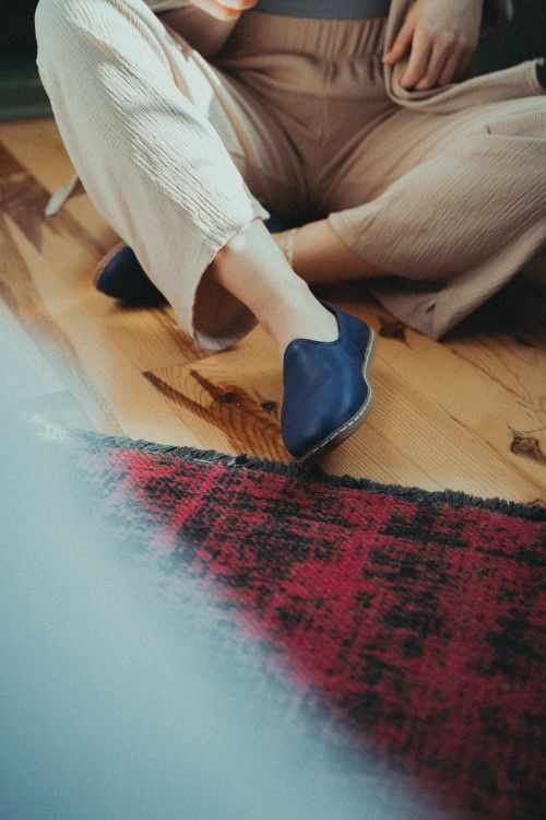 Free A woman sitting casually on a wooden floor with stylish shoes and elegant beige pants. Stock Photo