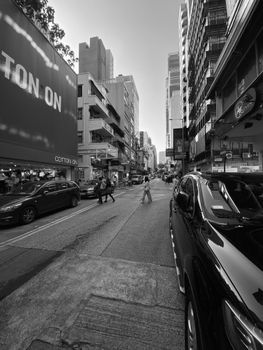 Black and white photo of a bustling city street with modern buildings and parked cars.