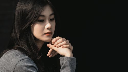 Free A thoughtful woman with dark hair gazes downward, her hands clasped elegantly. Stock Photo