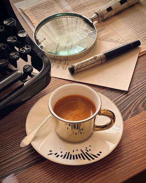 Golden Cup of Coffee on a Desk with a Typewriter and a Magnifying Glass