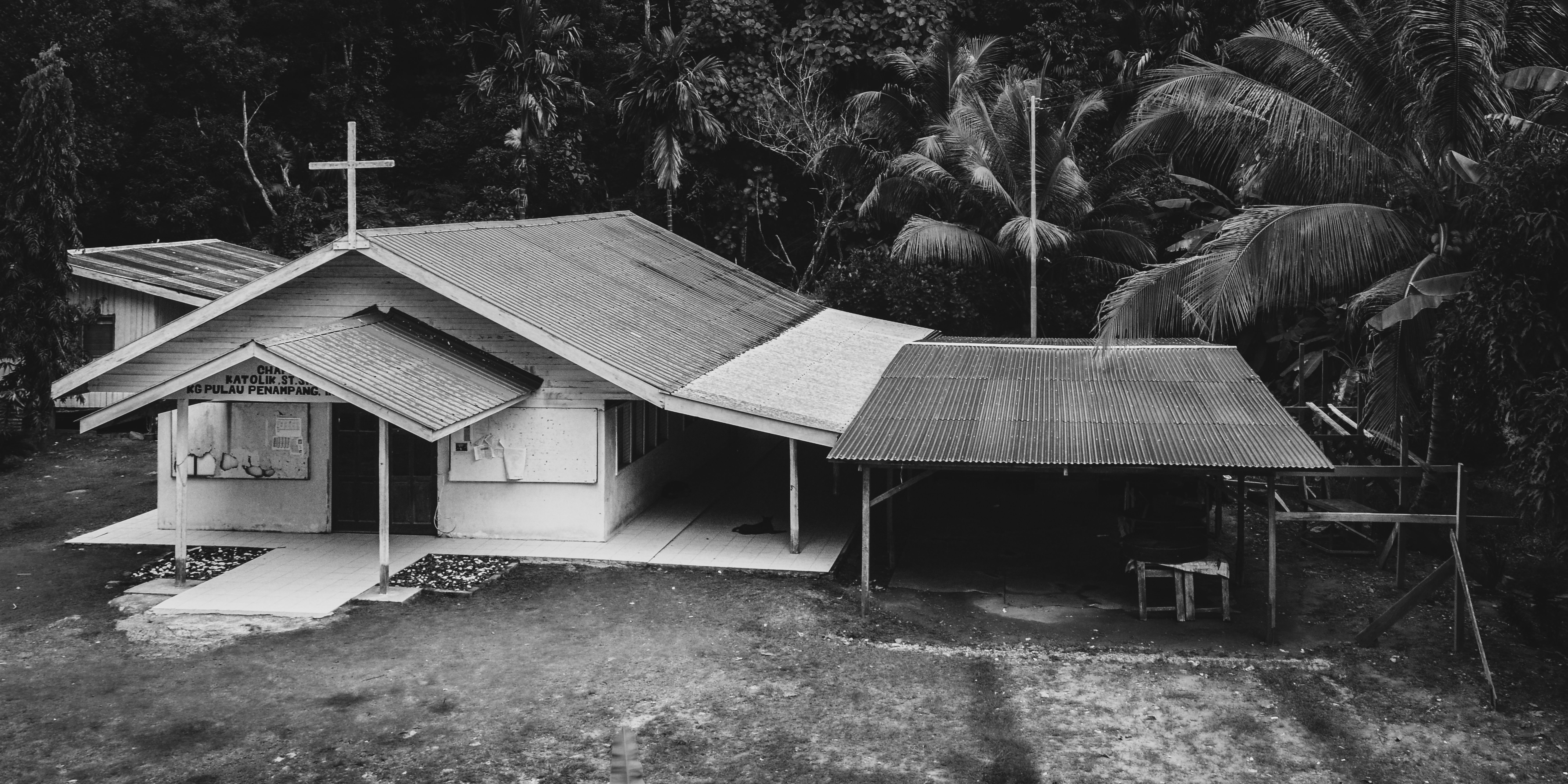 A serene black and white photo capturing a rural chapel surrounded by lush jungle vegetation.
