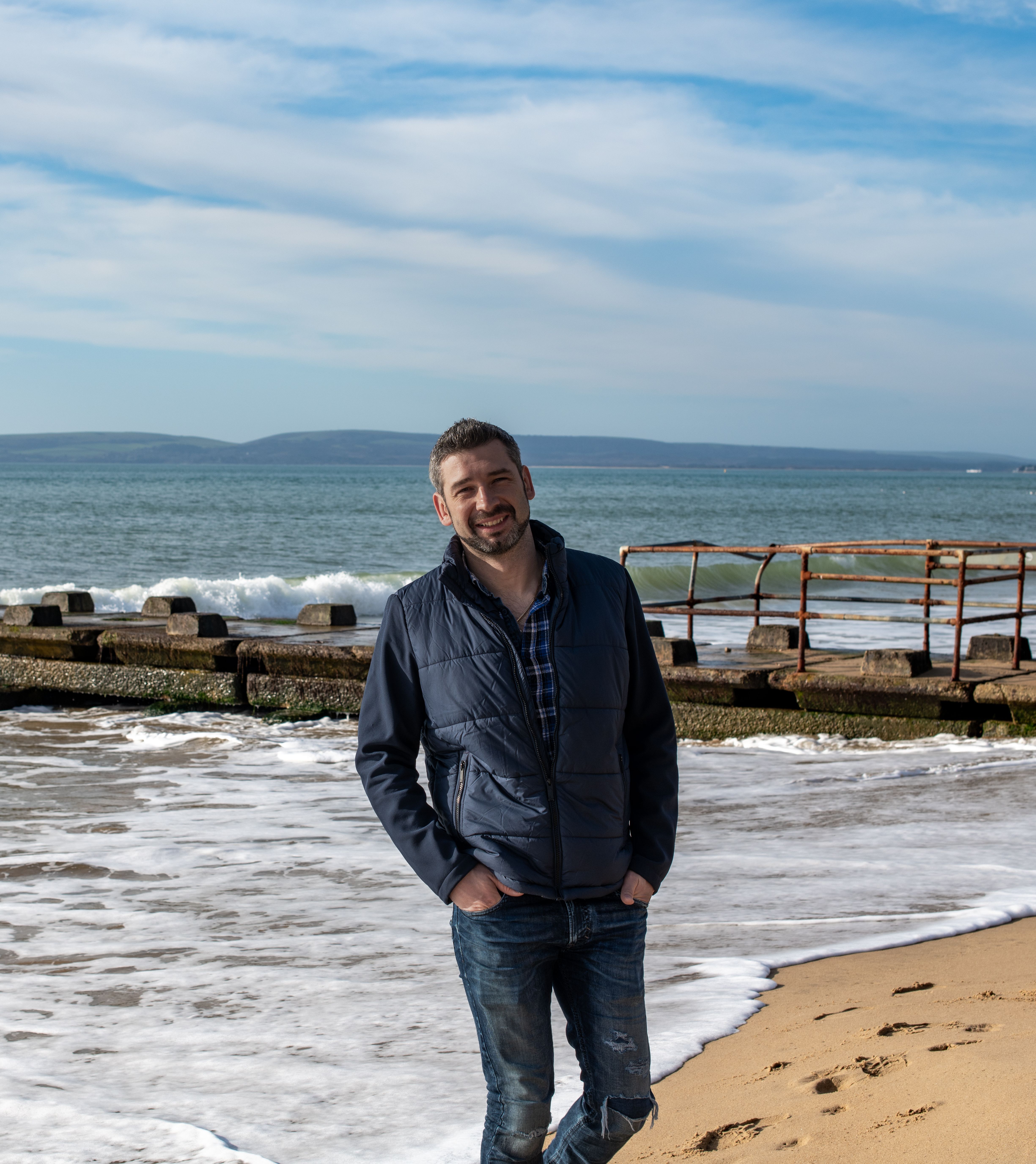 Cheerful man in casual outfit posing by the sea on Bournemouth beach, England.