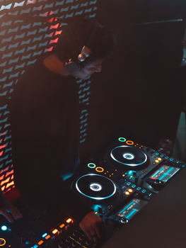 A DJ in a dark nightclub setting, mixing tracks with turntables and headphones.