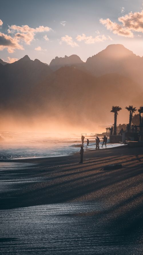 Free A stunning view of Antalya's coastline at sunset with mountains and palm trees silhouetted against the misty sky. Stock Photo