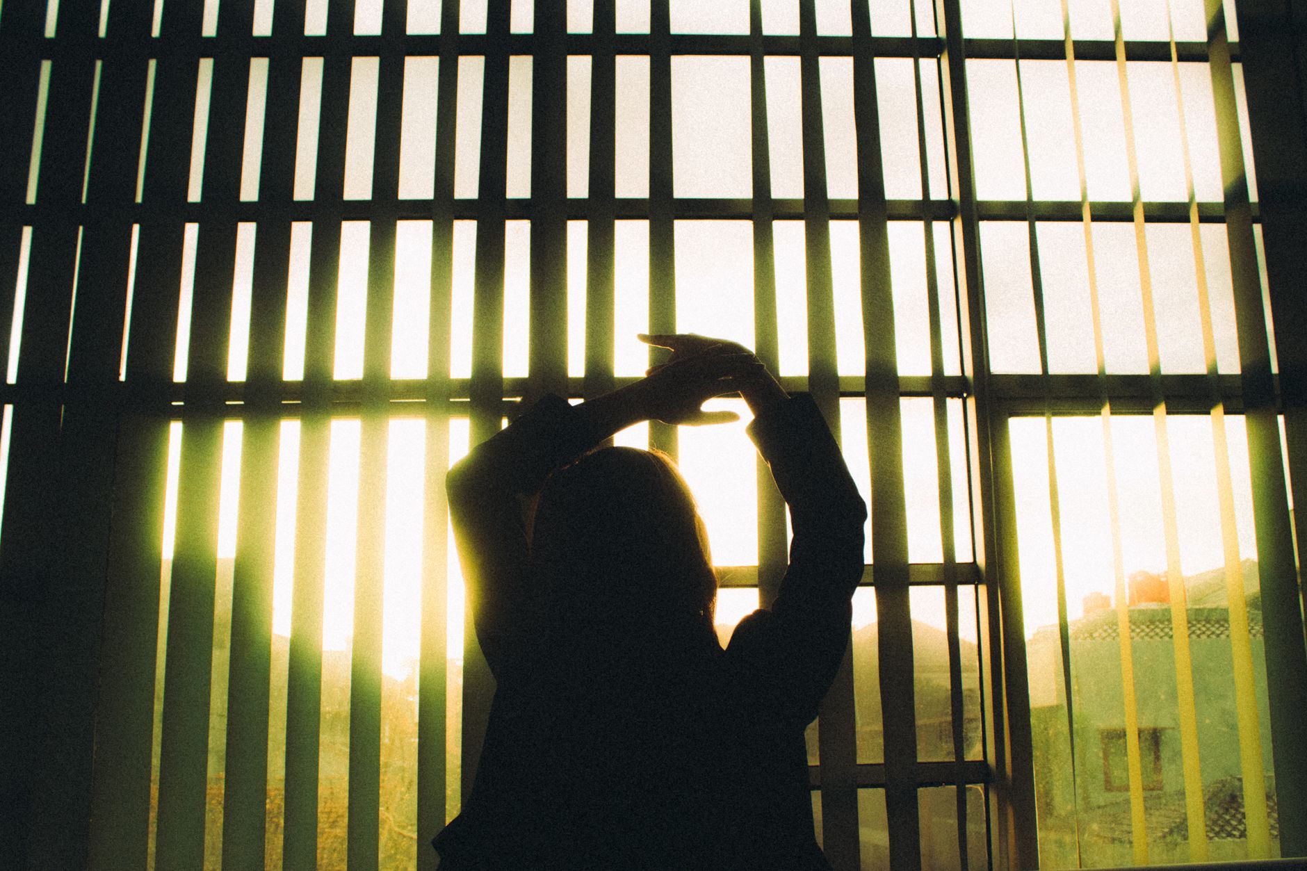窗邊太熱怎麼辦?不拆裝快速改善清單 Silhouette of a woman stretching in front of large window blinds with sunlight streaming in.