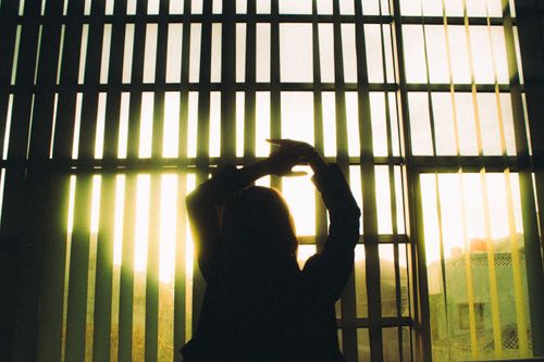 Free Silhouette of a woman stretching in front of large window blinds with sunlight streaming in. Stock Photo