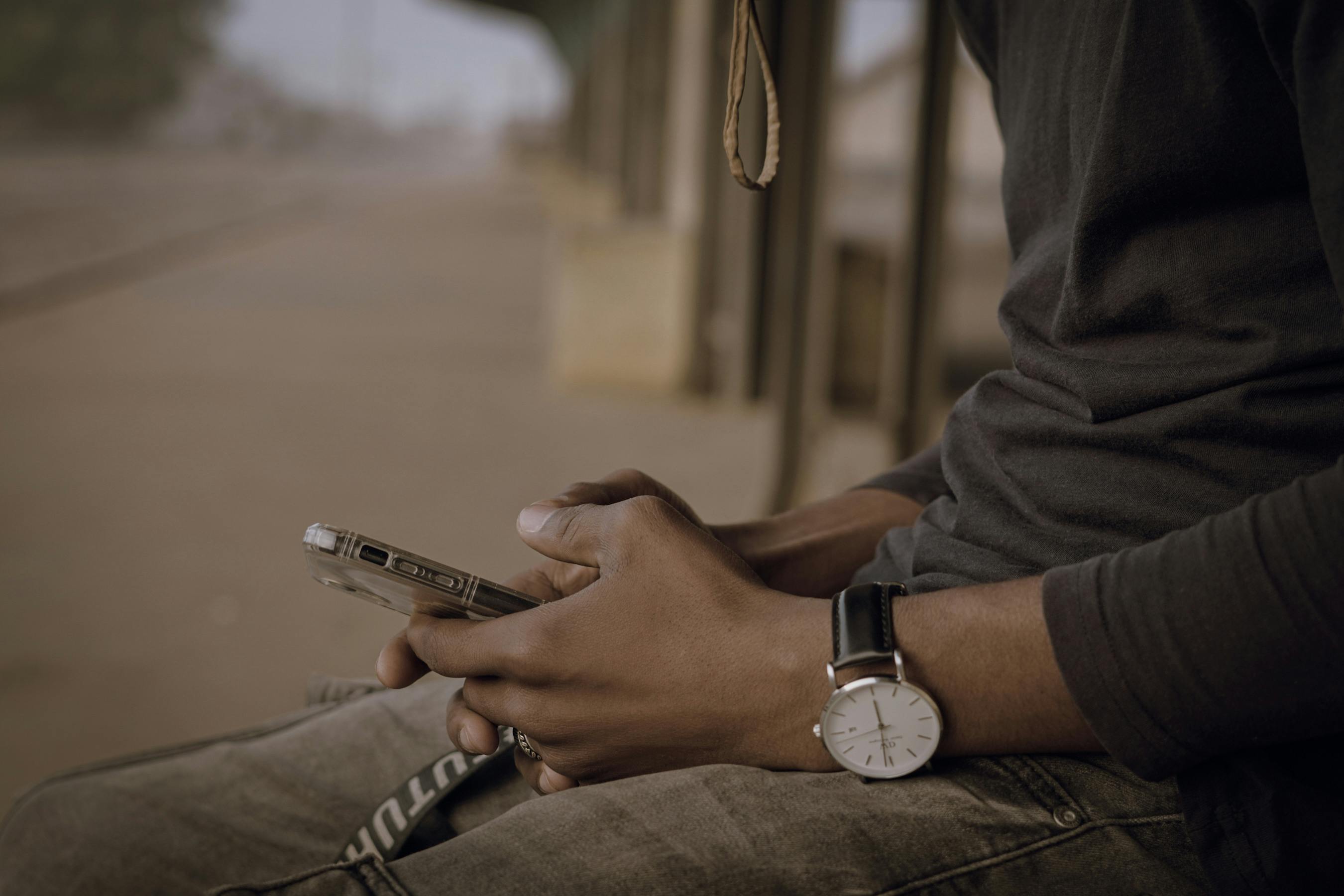 Close-up of a young man using a smartphone, sitting outdoors in Nigeria.