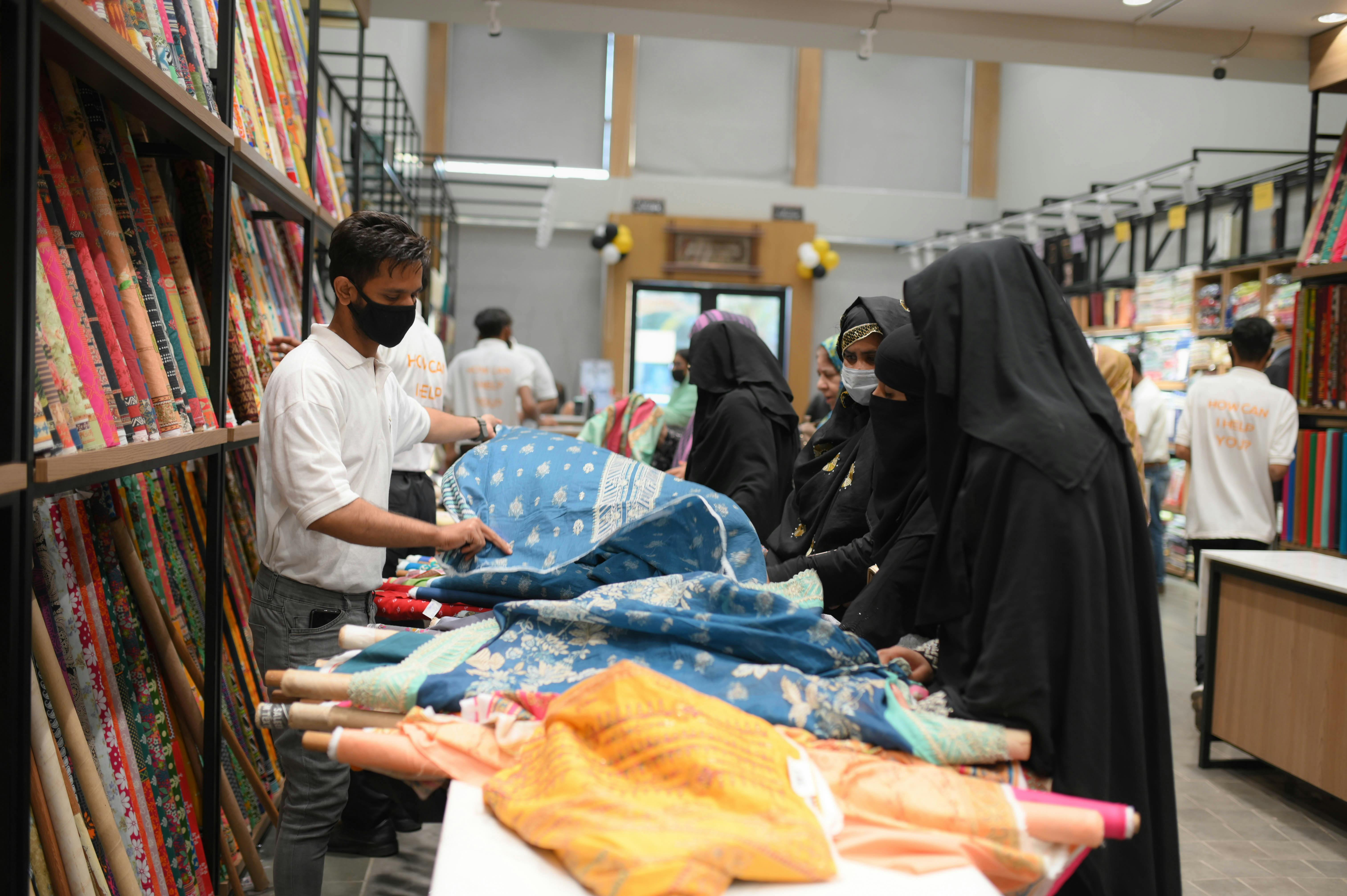 abaya website india - Women selecting colorful textiles in a fabric store, highlighting cultural attire.