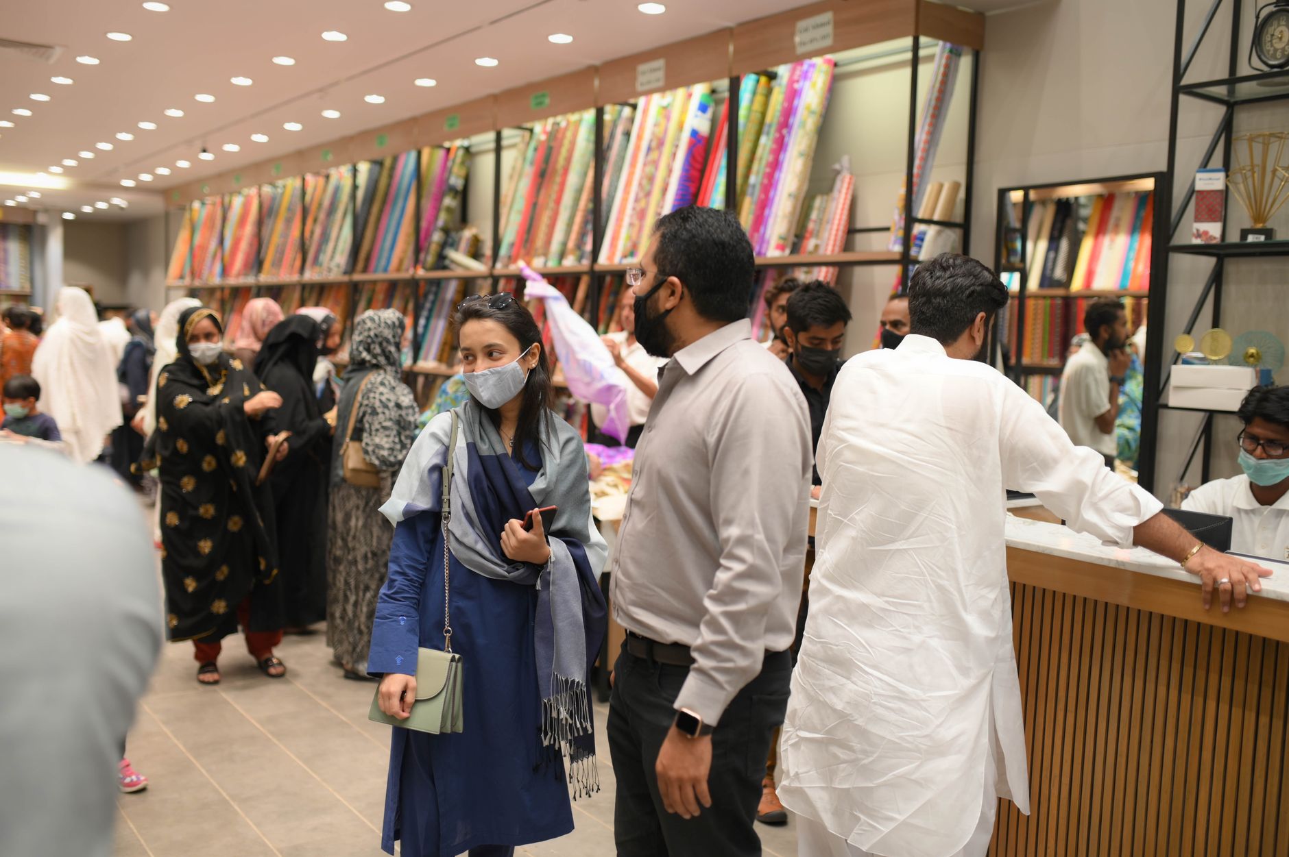 A bustling indoor fabric store with people shopping and browsing fabrics.