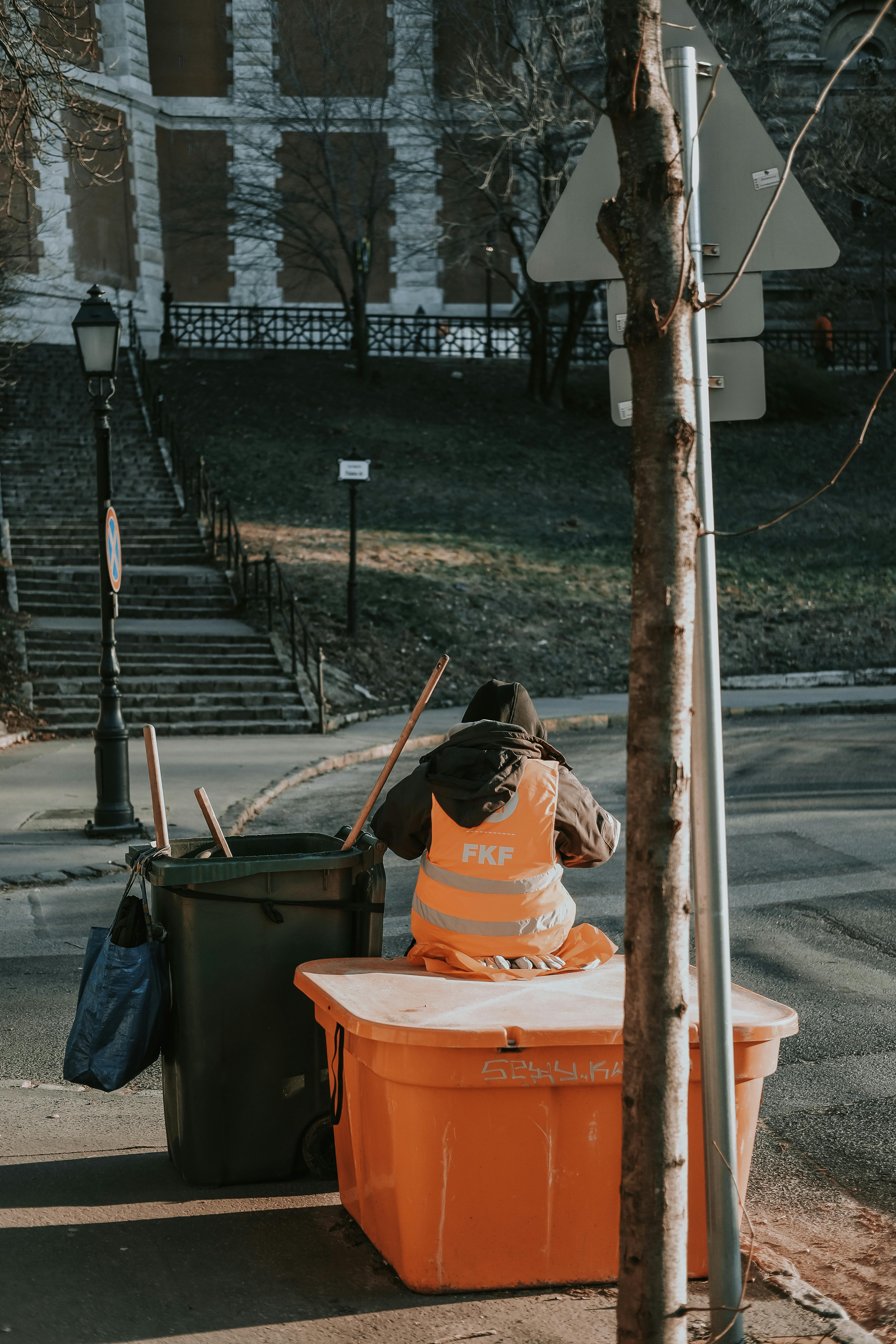 a man in orange vest sitting on a trash can