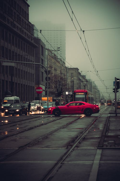 A red car driving down a street in the rain