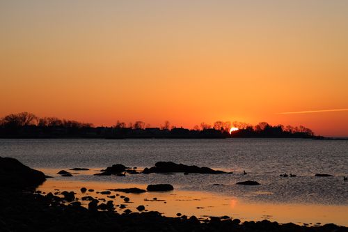 Free A calm seaside sunset showcasing silhouettes of a townline with gentle waves. Stock Photo