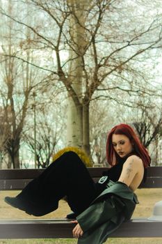 A fashionable woman with red hair posing on a bench in a tranquil winter park setting.