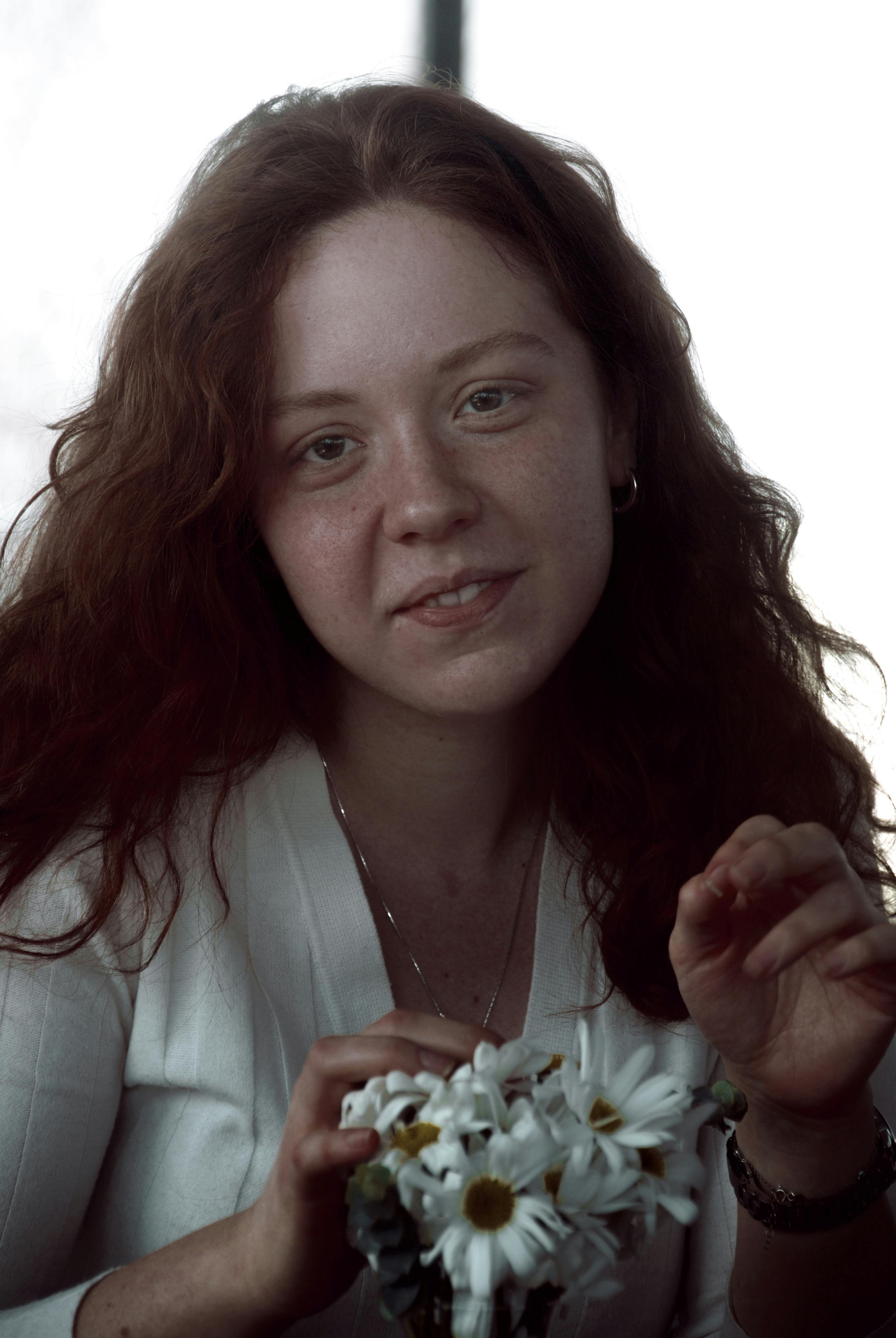 Portrait of a redhead woman holding a chamomile bouquet, featuring a warm and natural expression.