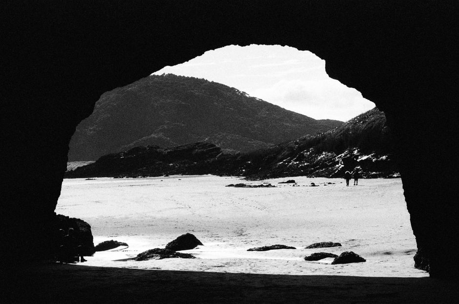 Monochrome view from inside a cave looking out to a serene beach.
