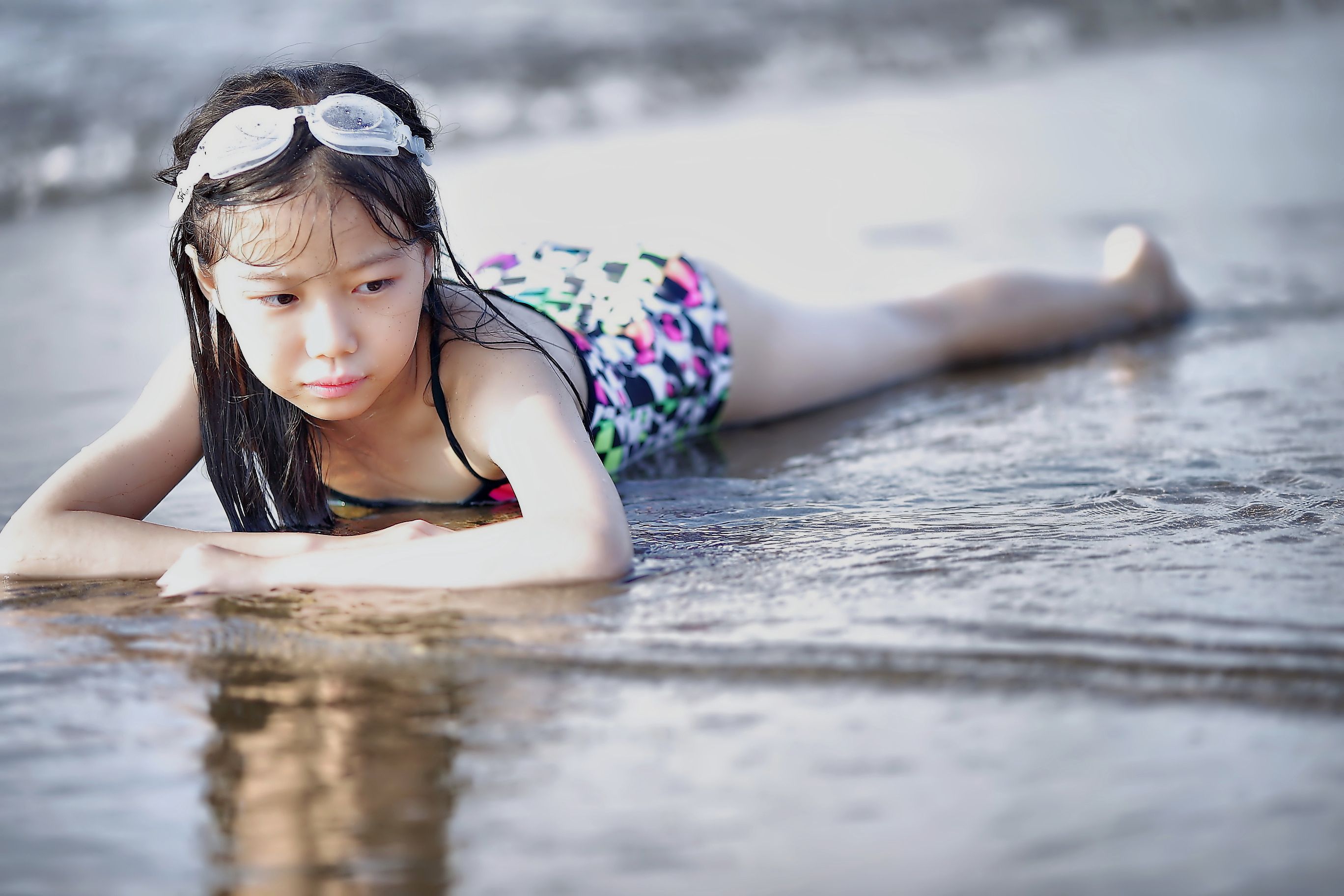 A young girl in swimwear enjoying a day at the beach, laying near the shoreline.
