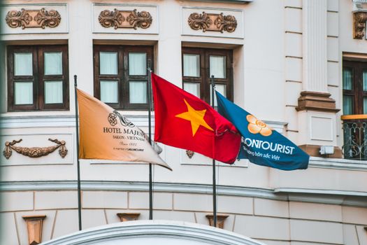 Flags of Vietnam and tourism on display at Hotel Majestic Saigon's facade.