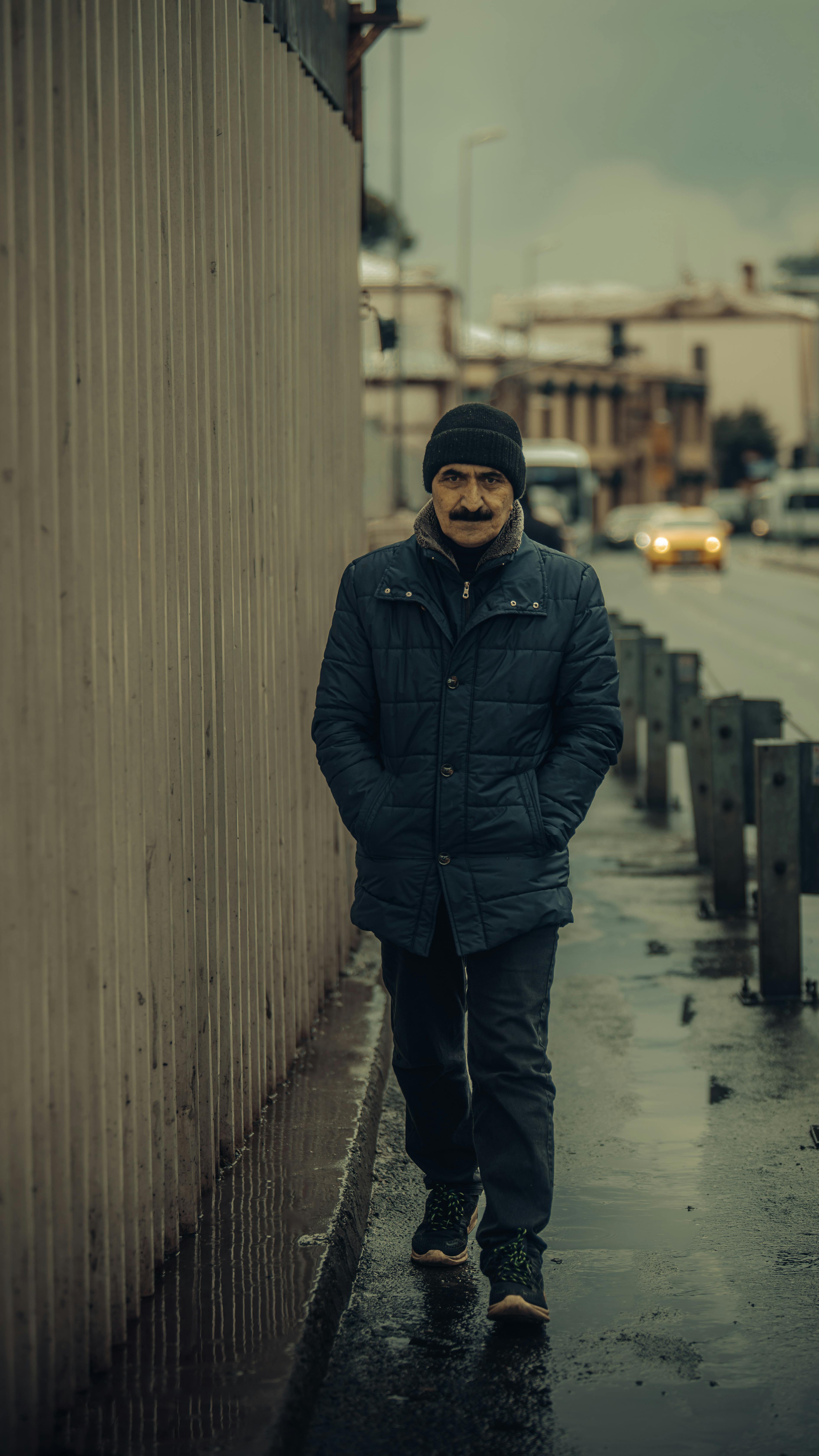 A man wearing warm clothing walks on a rainy sidewalk in Istanbul, Turkey.