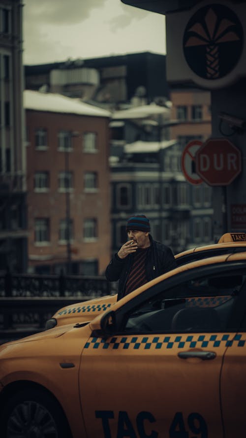 Man Standing next to a Taxi in City and Smoking a Cigarette 