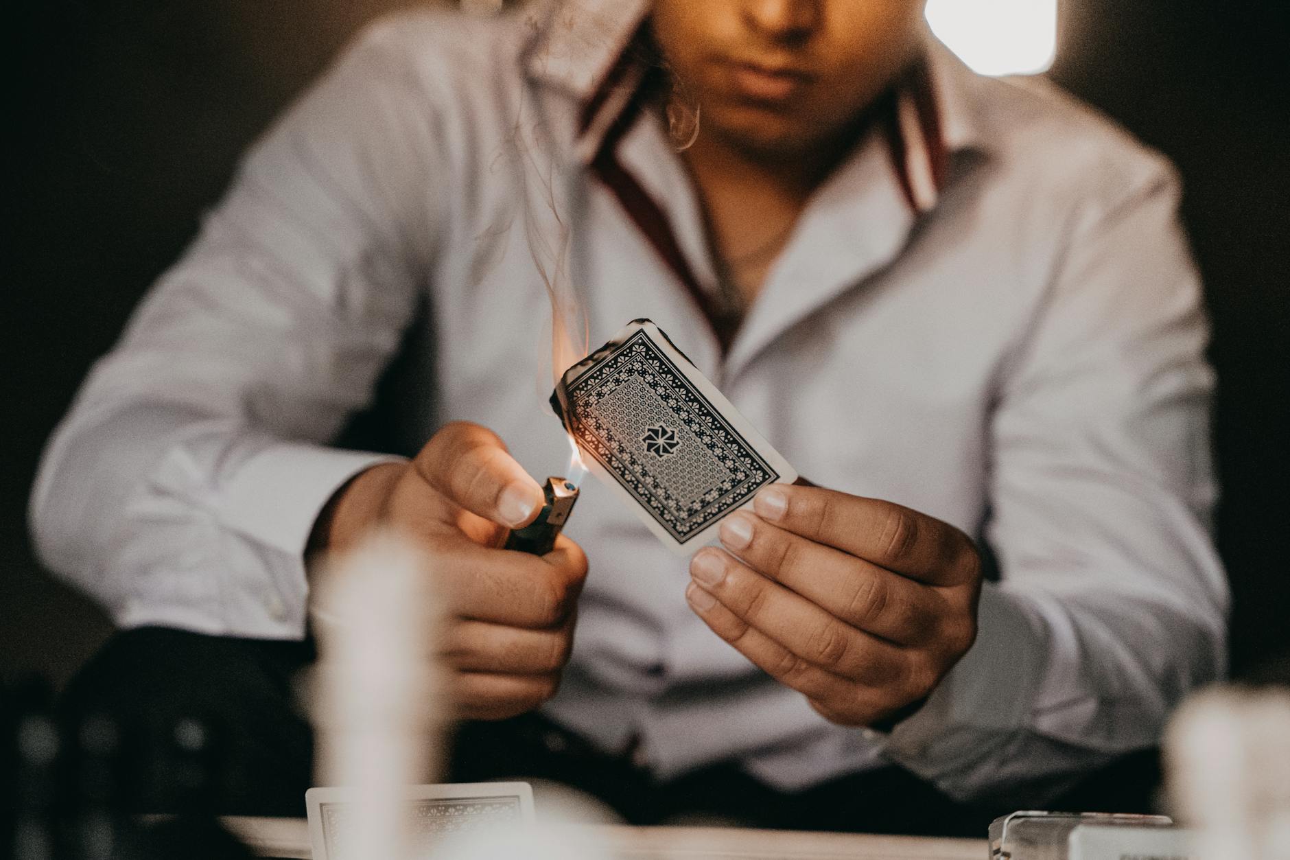 Close-up of a man setting a playing card on fire with a lighter indoors.