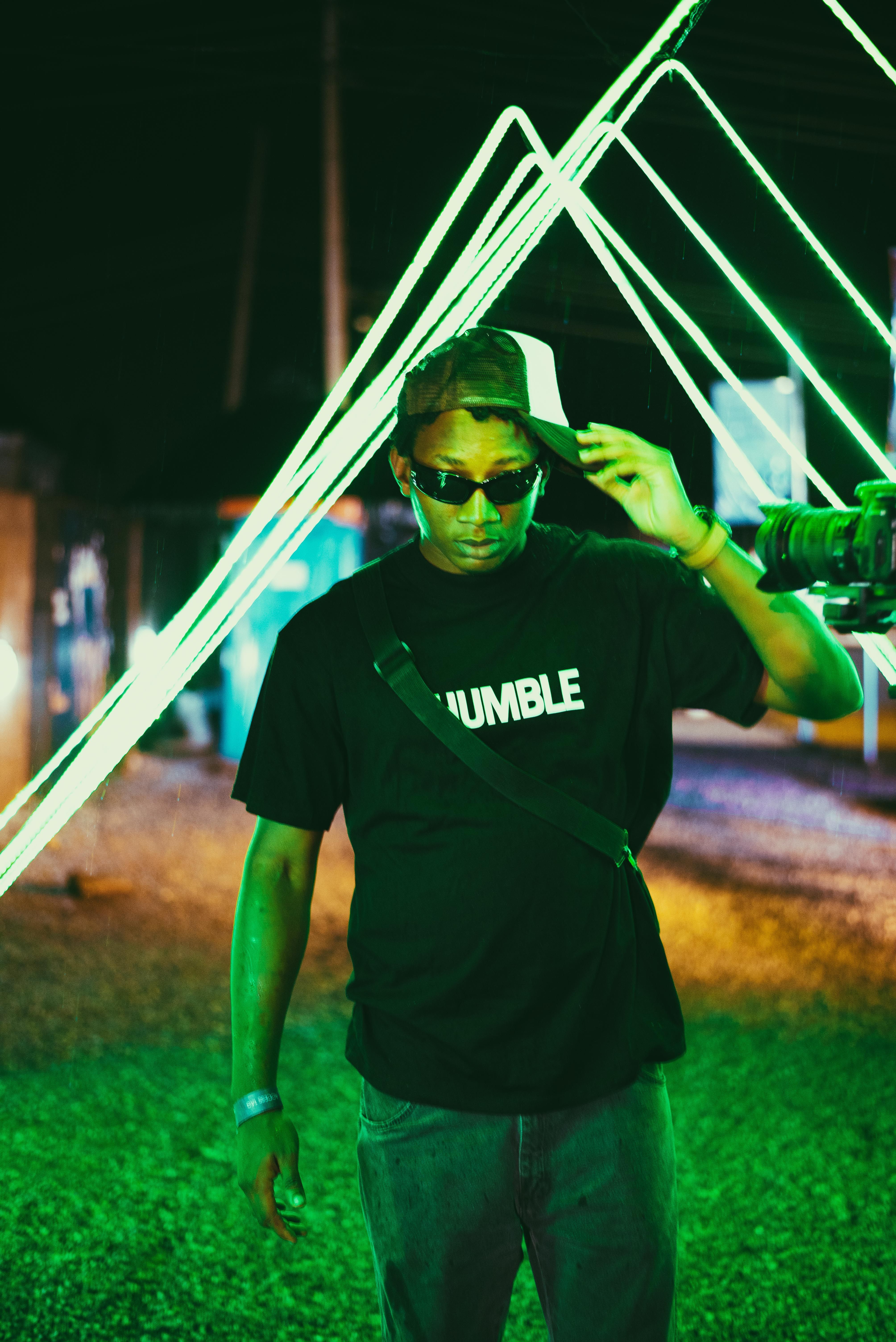 Trendy young man in sunglasses and cap enjoying a vibrant nightlife setting with neon green lights.
