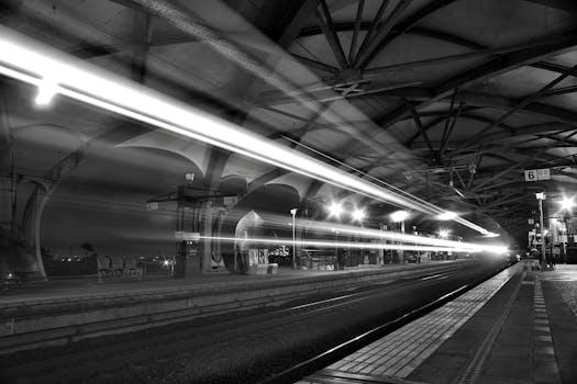 A long-exposure shot captures a train with light trails at a station platform during night time.