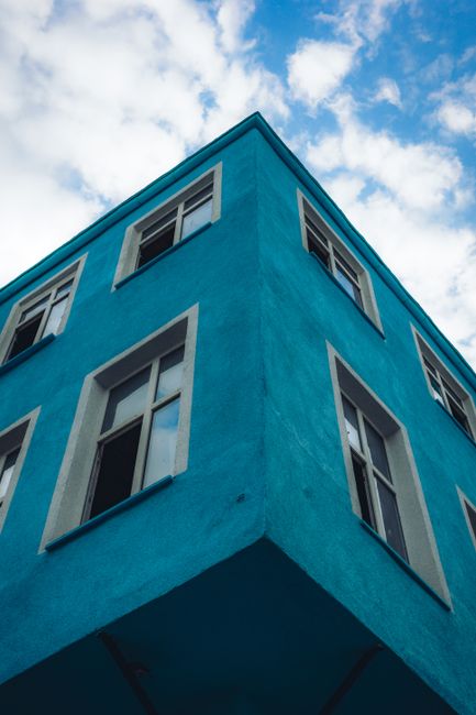 Low angle view of a bright blue building exterior with windows against a cloudy sky.